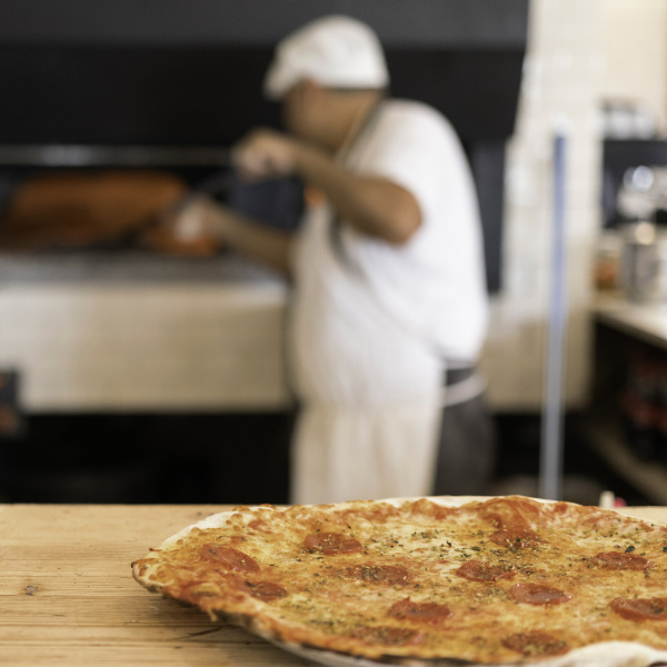 Pizza encima de una mesa y cocinero horneando pizzas