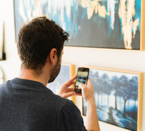 Persona joven tomando una fotografía de un cuadro con su teléfono